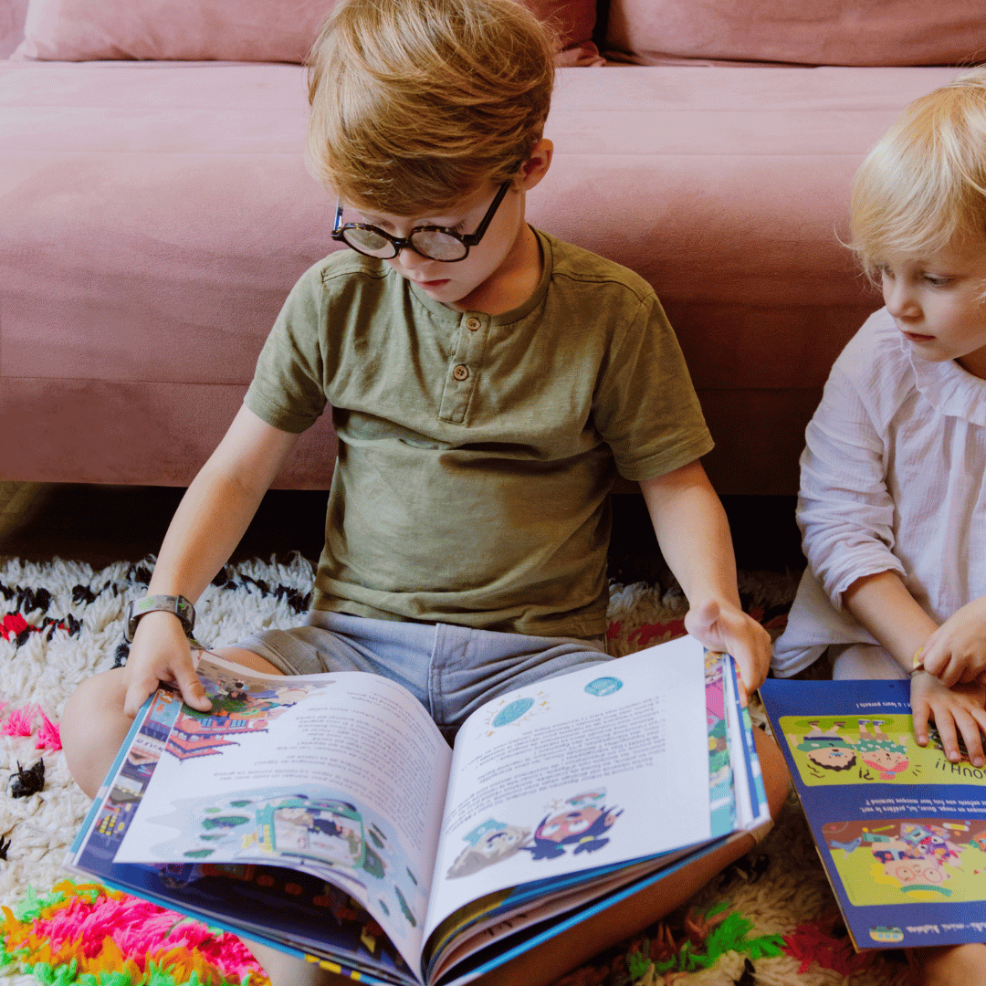 Un jeune garçon avec des lunettes explore un magazine éducatif, captivé par les illustrations et les histoires, accompagné d'une petite fille tenant un autre livre.