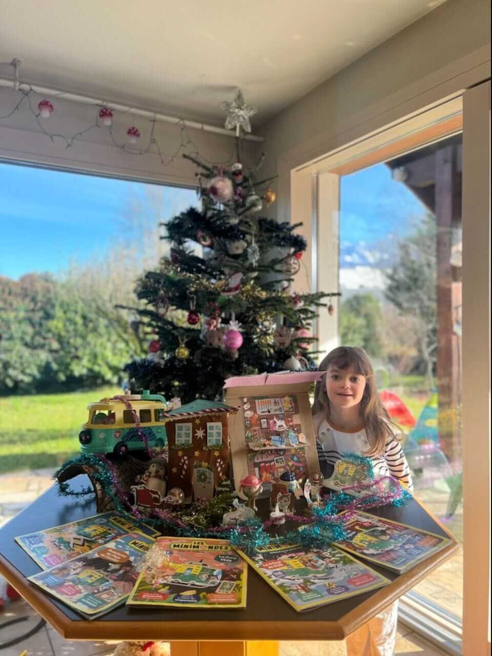 Une abonnée devant son sapin de noël avec le van, les magazines et sa magnifique maison du père noël fabriqué en carton