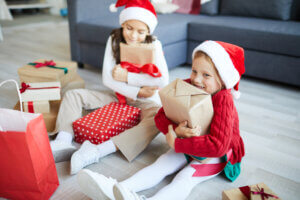 Deux enfants avec des bonnets de Noël souriants et tenant des cadeaux dans une ambiance festive.