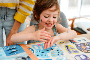 Fillette heureuse jouant avec des autocollants et découvrant un magazine éducatif.