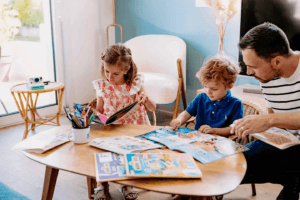 Un père partage un moment de lecture avec ses enfants autour de magazines éducatifs, favorisant la découverte et l’apprentissage en famille.