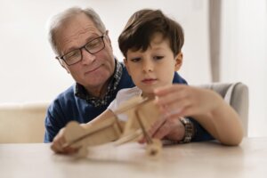 Un grand-père et son petit-fils assemblant un avion en bois pour apprendre en observant.